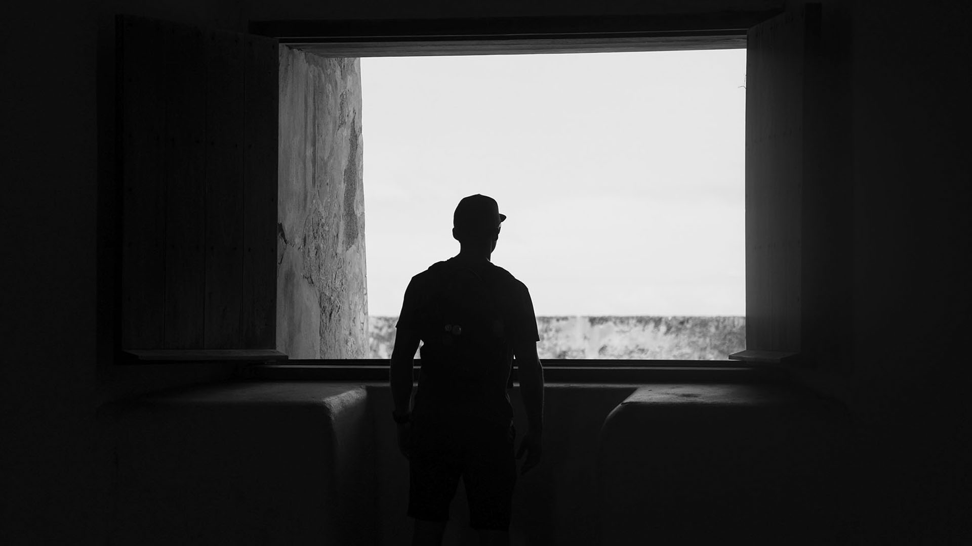 young man looking out a window in a dark room