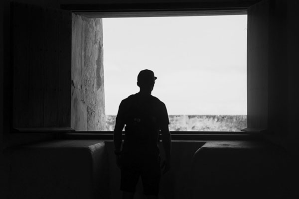 young man looking out a window in a dark room